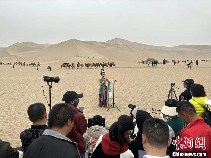 圖為2023年4月底，敦煌大漠“逐舞者”奧楠在鳴沙山月牙泉景區(qū)視頻直播，吸引游人圍觀?！●T志軍 攝